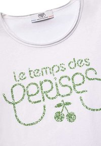 T-shirt en coton blanc avec un design de texte vert portant l'inscription "le temps des cerises" agrémenté de motifs floraux et de graphics de cerises. Encolure arrondie.