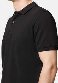 Czarna koszulka polo charakteryzuje się miękką teksturą, klasycznym kołnierzykiem, zapięciem na dwa guziki oraz krótkimi rękawami z przeszytymi brzegami, prezentując dopasowaną sylwetkę.