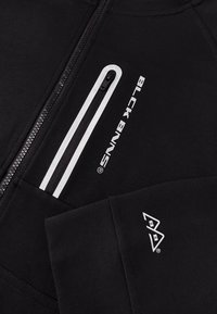 Zwarte sweatshirt met een rits, voorzien van witte accenten en logo-tekst. Zachte textuur, geribbelde manchetten en zakdetails.