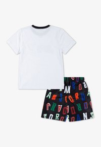 Camiseta blanca de algodón con cuello negro, combinada con pantalones cortos negros que presentan letras "JORDAN" en varios colores, fuentes y tamaños.