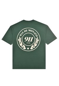 Mørkegrøn T-shirt med stort beige cirkulært logo på ryggen med teksten "PAS DE MONACO 911 CLUB" omgivet af laurbærgrene.