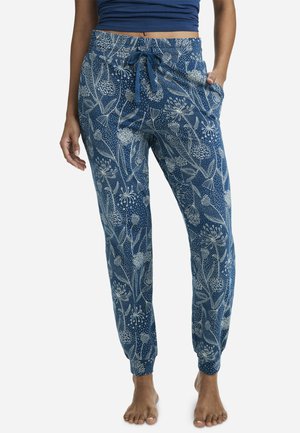 Woman wearing blue floral patterned drawstring jogger pants with cuffed ankles, paired with a blue crop top, standing barefoot.