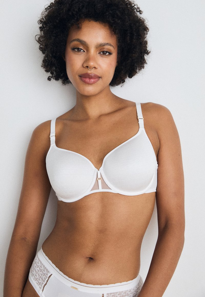 White bra with smooth cups, adjustable straps, and a mesh center panel. Features a gold-tone accent at the front.