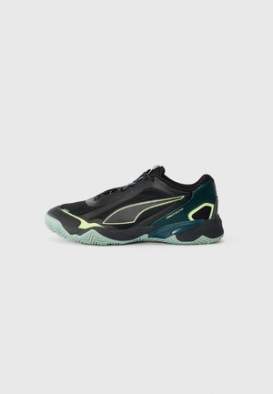 Black athletic shoes with a textured mesh upper, teal accents, and a flexible green sole featuring a zigzag pattern. Laces and reinforced toe box.