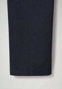 Marineblauwe stof bij de beenopening met een nette zoom. De textuur lijkt zacht, met een eenvoudig design zonder extra patronen of accenten.