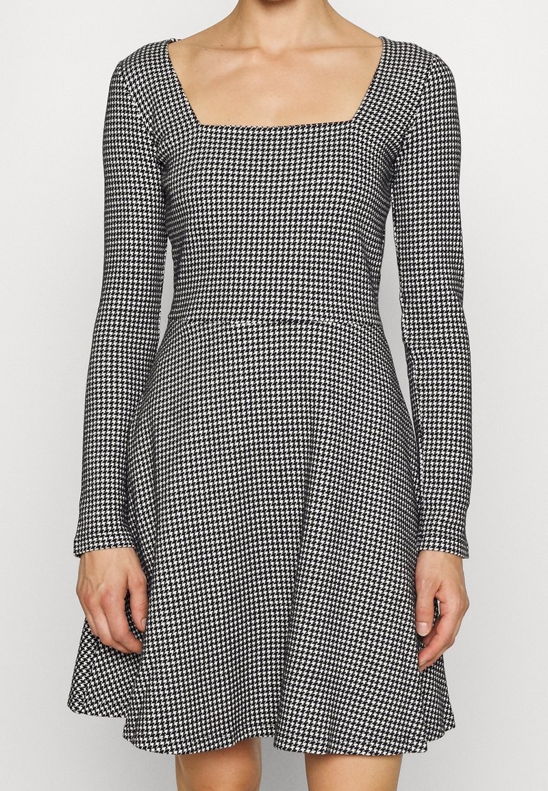 Schwarz-weißer karierten Kleid mit quadratischem Ausschnitt, langen Ärmeln, tailliertem Oberteil und ausgestellten Rock, aus dehnbarem Stoff.