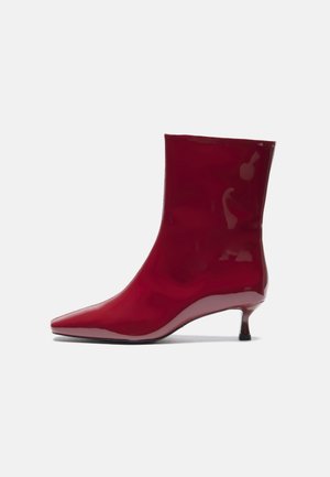 Bottine en cuir verni rouge avec un bout pointu et un talon court et fin, présentant une surface lisse et brillante ainsi qu'un design minimaliste.