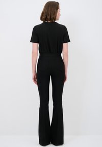Zwart kortom shirt gedragen met hoge taille zwarte flared broek met achterzakken en een gladde textuur. Effen kleur over de gehele outfit.