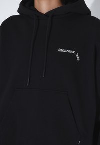 Felpa nera con tasca frontale, cappuccio con lacci e testo ricamato bianco che recita "GOOD TIMES" sul lato sinistro del petto. Tessuto morbido.