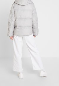 Šedá puffer bunda s kapucí, zdobená prošívaným designem. Kombinována s bílými kalhotami širokého střihu a bílými teniskami. Měkká textura a volný střih.