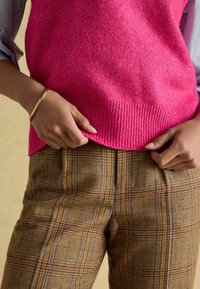 Fuksia kudumüts ribitud servaga, mis on kaunistatud tekstuursete pruunide ruuduliste pükste ning peenete siniste ja punaste triipudega. Käel kuldne käevõru.