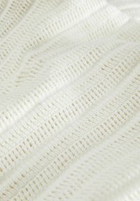 Pletená bílá textilie s texturovaným cik-cak vzorem, obsahující otevřené tkaninové úseky a měkký, vláknitý vzhled.