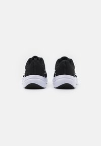 Scarpe da ginnastica nere con una parte superiore in mesh testurizzato, suola intermedia bianca e suola esterna nera. Presentano un design semplice con un branding minimale.
