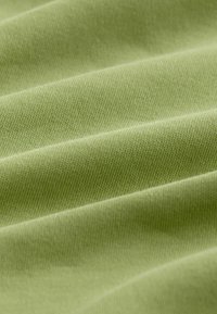 Világoszöld szövet, sima, enyhén texturált szövésű, lágy redőkkel és egyenletes színnel az egész felületen.