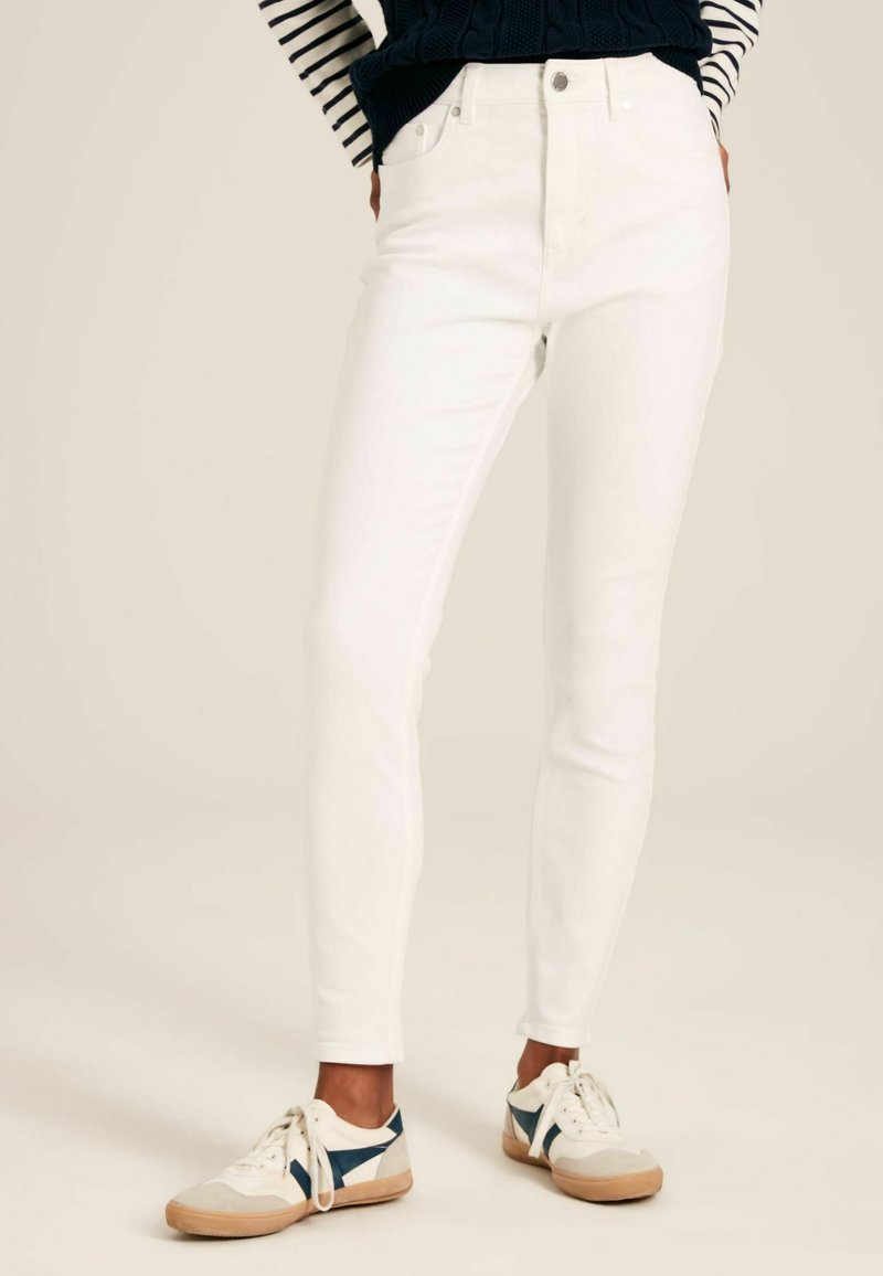 Valged denimi skinny teksad kõrge vöökoht, mis on varustatud luku ja viie taskuga ning sujuva tekstuuriga, koos mugavate spordijalatsitega.