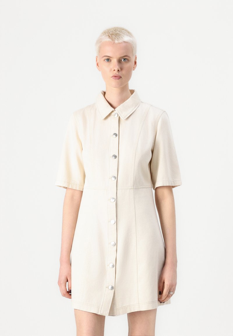 Robe à manches courtes en tissu beige clair, dotée d'une fermeture à boutons sur le devant avec des boutons argentés et un col.