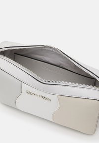 Saszetka Calvin Klein z szarej i białej skóry, o gładkiej fakturze, zamknięcie na zamek oraz srebrne logo. Wnętrze jest eleganckie i proste.