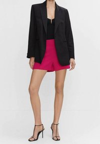 Zwarte blazer over een zwarte top, gecombineerd met felroze shorts en zwarte strappy hoge hakken. Eenvoudig ontwerp, op maat gemaakt.