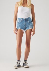 Högmidjade jeansshorts i ljusblått med fransiga kanter och slitna detaljer; kombinerade med en vit linne och marinblå höga sneakers.