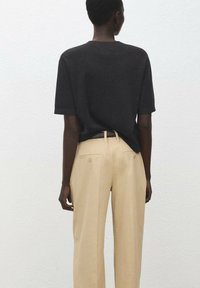 Czarna koszulka krótki rękaw w połączeniu z beżowymi spodniami z wysokim stanem. Koszulka ma luźny krój; spodnie posiadają boczne kieszenie i detale z guzikami.