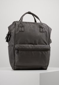 Šedý nylonový batoh s dvojitými horními uchy, přední kapsou na zip, texturovaným povrchem a nenápadnou značkovou nálepkou. Čtvercový tvar s vyztuženým švem.