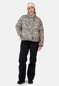 Kurtka puchowa w panterkę z wysokim kołnierzem, czarnymi akcentami i elastycznymi mankietami, zestawiona z czarnymi spodniami i jasną wełnianą czapką.