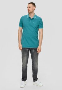 Tyrkysové polo tričko s límcem na dva knoflíky, bílým lemem a detailním logem, spárované s vybledlými šedými džíny a bílými teniskami.