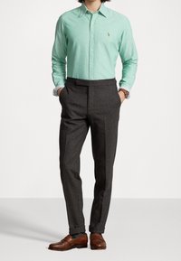 Ljusgrön, långärmad skjorta med knappar och krage, kombinerad med mörkgrå skräddarsydda byxor och bruna slip-on skor.