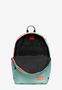Mochila de color aguamarina con detalles rojos y un diseño a rayas. El interior abierto presenta un forro negro, múltiples compartimentos y una etiqueta de marca.