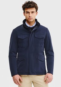 Granatowa kurtka wykonana z gładkiego materiału, charakteryzująca się wysokim kołnierzem, czterema kieszeniami z przodu oraz zapięciem na zamek, zaprojektowana z myślą o dopasowanym kroju.