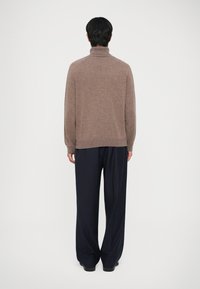 Brown knit turtleneck sweater paired with navy pinstriped wide-leg trousers. The sweater features a relaxed fit and ribbed hem detailing.