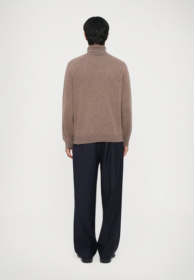 Un pull à col roulé en tricot brun associé à un pantalon large à rayures marines. Le pull présente une coupe décontractée et des détails de bord côtelé.