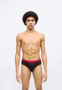 Μαύρο βαμβακερό σλιπ με κόκκινη ελαστική ζώνη μέσης που φέρει το λογότυπο "TOMMY HILFIGER". Ομαλή υφή, εφαρμοστό σχέδιο και κλασική κοπή.