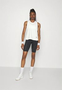 Biała sportowa koszulka bez rękawów, czarne dopasowane spodenki z perforowanym wzorem, białe trampki i opaski na nadgarstki. Prosty, sportowy design.