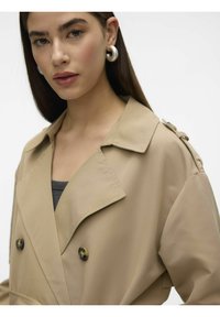 Beige dobbeltspent trench coat med stort krage og knappdetaljer. Glatt tekstur, med skulderstropper og en avslappet passform.