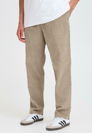Pantaloni in corduroy color tan con righe verticali, a vestibilità rilassata e tasche laterali. Abbinati a sneakers bianche e grigie con strisce nere.