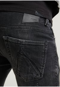 Svarta denimjeans med slitna detaljer, en lädermärke på midjan och distinkta formade bakfickor.