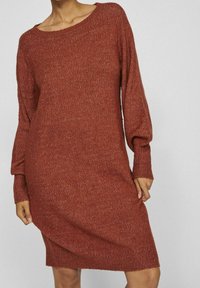 Robe pull couleur rouille avec une coupe décontractée, manches longues, encolure ronde large et tissu en maille texturée. Longueur mi-cuisse.