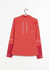 Röd, långärmad träningsskjorta med reflexremsor, hög krage och texturerat tyg, hängande på en svart krok.