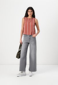 Rødstribet ærmeløs top parret med højtaljede grå vide jeans. Modellen holder en mørkegrøn håndtaske og bærer hvide sneakers.