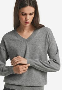 Grauer V-Ausschnitt-Pullover mit langen Ärmeln und gerippten Bündchen, aus weichem Strickstoff gefertigt, mit einer lockeren Passform und minimalen Nähten.