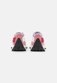 Chaussures de sport rétro avec une tige en daim rose, des superpositions blanches et une semelle extérieure en caoutchouc noir texturé avec une forme triangulaire distinctive.
