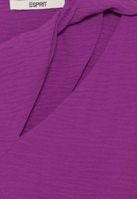 Top morado de Esprit con un tejido suave y texturizado; presenta un escote en V y un diseño drapeado, que enfatiza líneas fluidas y detalles de costura simples.