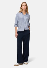 Blue and white striped button-up shirt with rolled sleeves, paired with navy wide-leg pants and white sneakers with brown soles.
