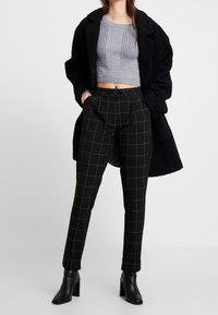 Czarne spodnie w kratę o dopasowanym kroju, szary prążkowany krótki sweter oraz czarny oversize'owy płaszcz. Do tego stylizacji dobrano czarne botki na obcasie.