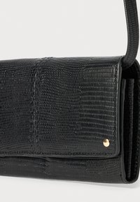 Black textured handbag made of synthetic material. Features a subtle reptile pattern, gold accent stud, and a shoulder strap.