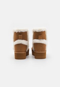Ruske nubuk ankle boots z belim umetnim krznom, kvadratnim zadnjim delom, ravnim rjavim podplatom in majhno peto, s trakcem za enostavno obuvanje.