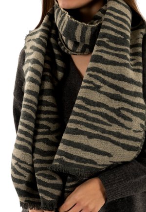 Bufanda beige con rayas de tigre en gris oscuro, bordes con flecos, envuelta alrededor del cuello, hecha de material suave, usada sobre un suéter oscuro.