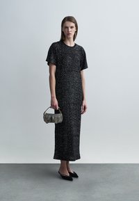 Μακρύ μαύρο φόρεμα με γκλίτερ και κοντά μανίκια, σε συνδυασμό με υφασμάτινη γκρι τσάντα. Το μοντέλο φοράει μαύρες μυτερές μπαλαρίνες. Απλή, κομψή σιλουέτα.