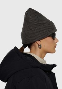 Szara prążkowana czapka z dziubkiem, w zestawie z czarną puchową kurtką, beżowym kołnierzem i czarnymi okularami przeciwsłonecznymi; ozdobiona okrągłymi srebrnymi kolczykami.